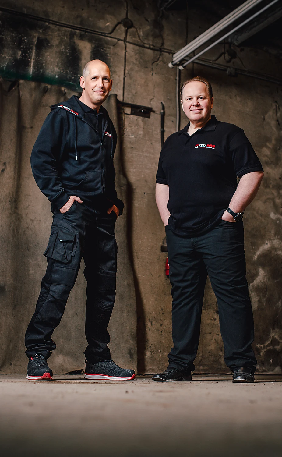 Frank Roß und Thomas Meßner die beiden Inhaber von dem Fliesenleger Meisterbetrieb Keranovo aus Düren tragen Kleidung mit Keranovo-Schriftzug und lächeln aufrecht stehend in die Kamera.